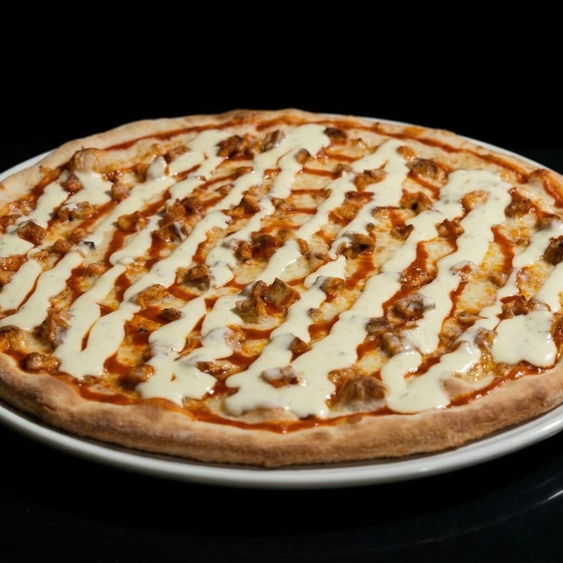 Pompeii Pizzeria's chicken pizza, drizzled with white sauce and red sauce, on a white plate.