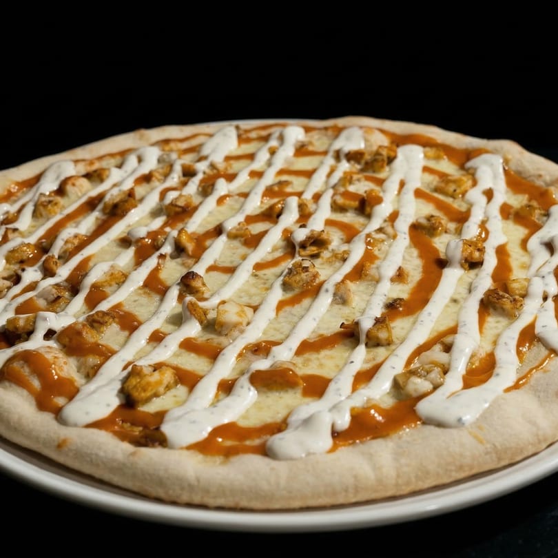 A Pompeii Pizzeria pizza with chicken, cheese, and a drizzle of orange and white sauces.